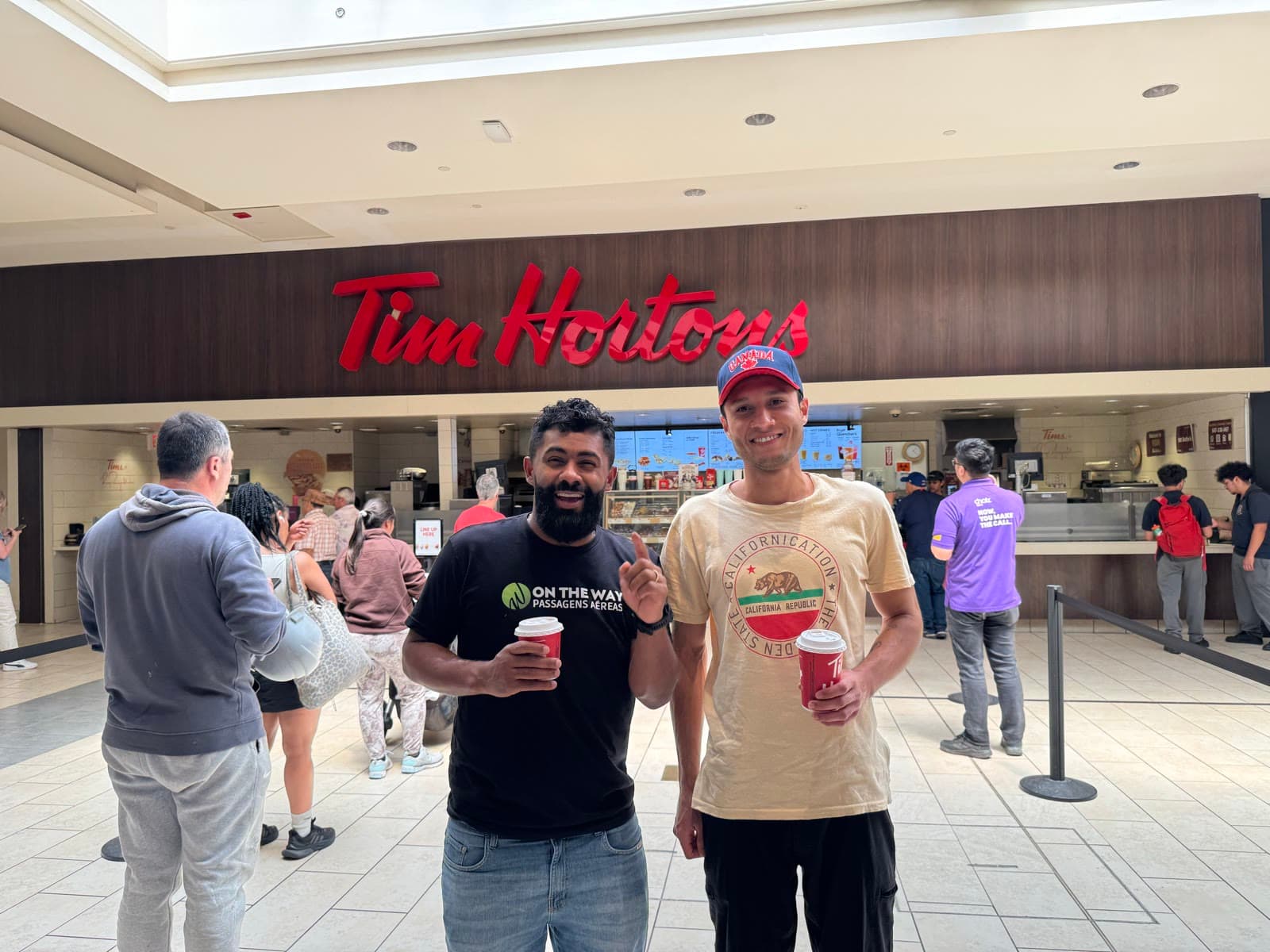 Duas pessoas segurando copos em frente ao balcão de uma lanchonete Tim Hortons