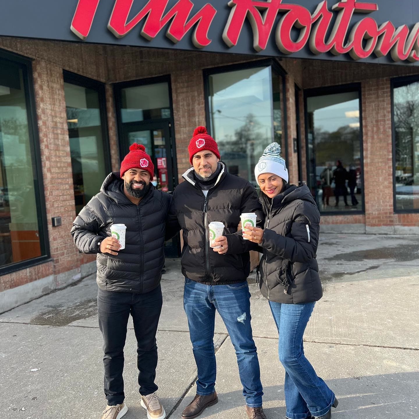 Três pessoas com gorros e copos em frente a uma lanchonete Tim Hortons